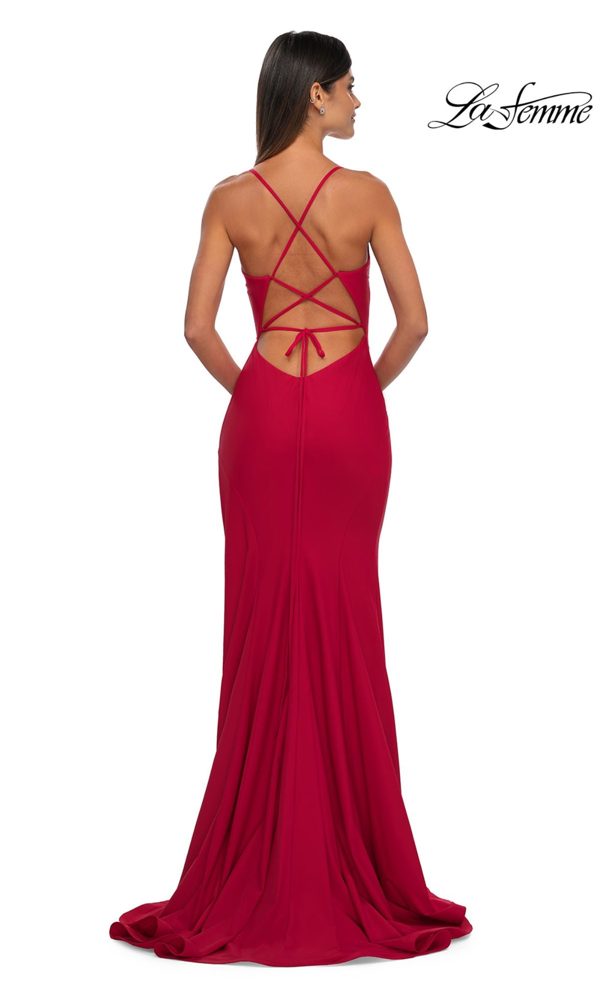 A woman wearing the Classic Long V-Neck Prom Dress: La Femme 33080, a floor-length fitted red gown with an open cross-strap back and bow detail, stands against a plain white background.